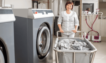 Staff member with laundry cart next to commercial laundry equipment.