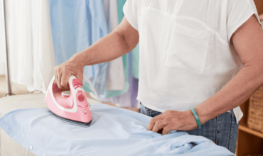 Older woman using a pink automatic ironing machine on a blue shirt in a well-lit room