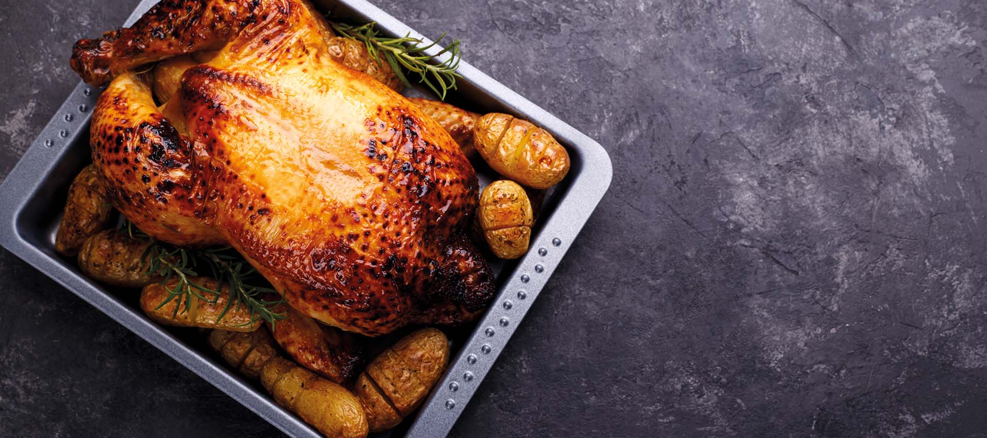 Roasted chicken with potatoes in a tray, prepared in a facility featuring commercial laundry equipment like commercial tumble dryers and automatic ironing machines