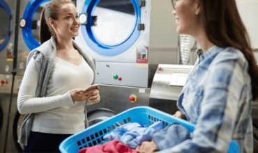 Two women chatting in a laundromat with Electrolux Commercial Laundry Equipment in the background.