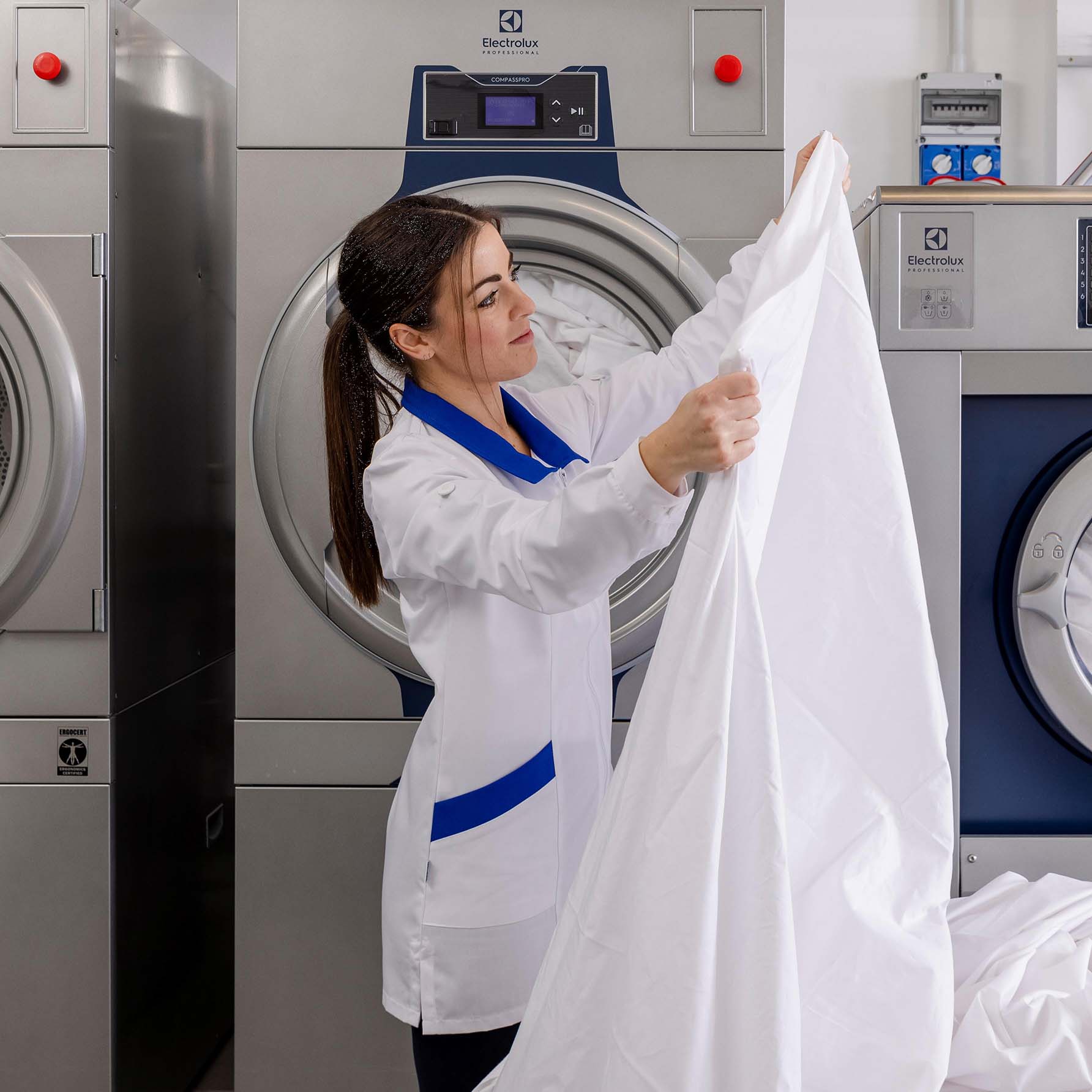 Employee folding laundry near commercial washer and dryer