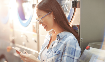 Person using a phone near commercial washer machines.